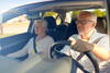 a older man driving his car with an older woman in the front passenger seat